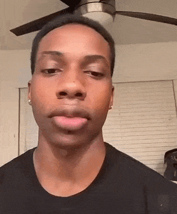a young man is making a funny face in front of a ceiling fan in a living room .