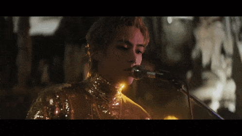 a woman singing into a microphone while wearing a gold dress