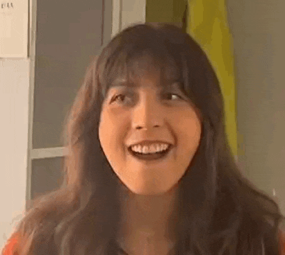 a woman with long hair and bangs is smiling and looking at the camera with her mouth open .