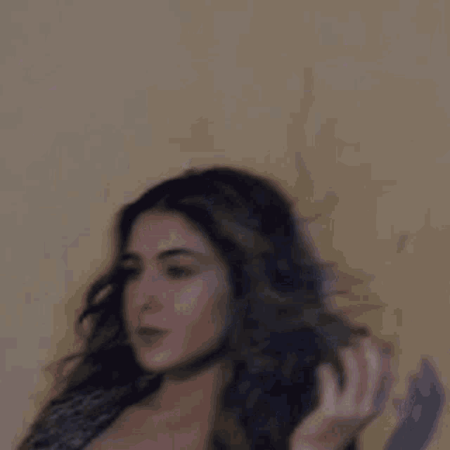 a woman with long hair is standing in front of a wall holding her hair .
