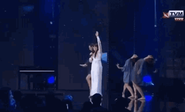 a woman in a white dress is singing into a microphone on stage