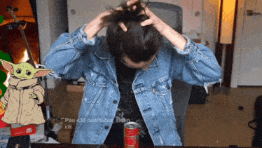 a person in a denim jacket is sitting at a desk with a can of coke in front of them
