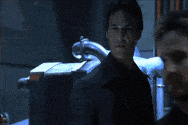 a man in a suit stands in a dark room with a blue light behind him