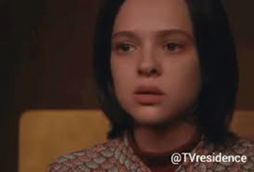 a close up of a woman 's face with a surprised look on her face while sitting in a chair .