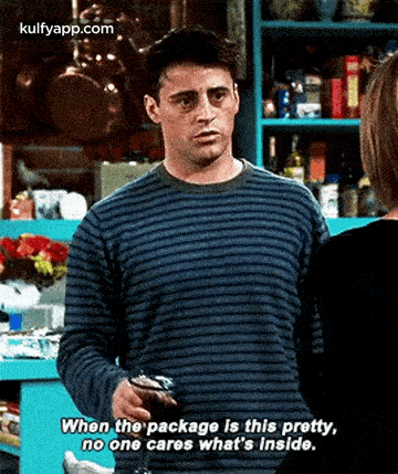 a man in a striped sweater is talking to a woman in a kitchen while holding a wallet .