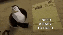 a stuffed penguin is standing next to a cardboard box that says `` i need a baby to hold ''