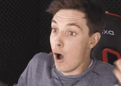 a young man is sitting in a chair with his mouth open and making a surprised face .