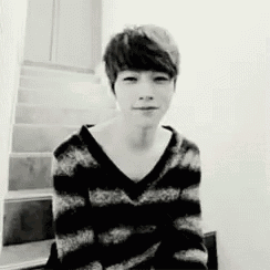 a black and white photo of a young man wearing a striped sweater sitting on a staircase .