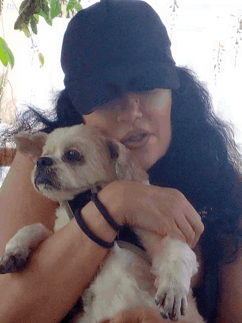 a woman in a black hat holds a small white dog