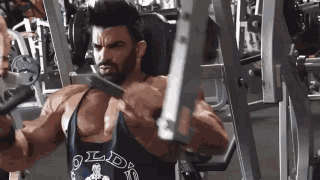 a man is using a machine in a gym while wearing a gold's gym tank top .