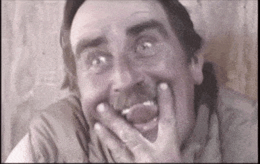 a man with a mustache is making a funny face with his hands on his face .
