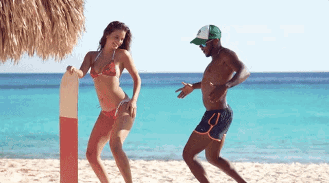 a man and a woman are dancing on the beach and the woman is wearing a bikini and holding a surfboard