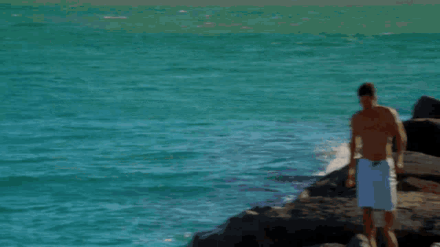 a shirtless man in white shorts walks along the beach