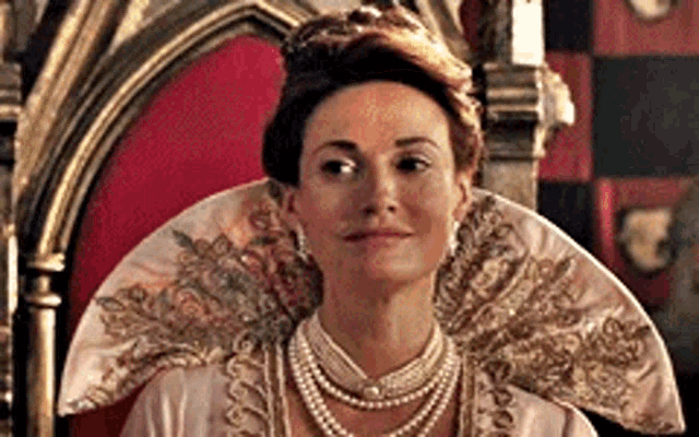 a woman is sitting on a throne wearing a tiara and pearls .