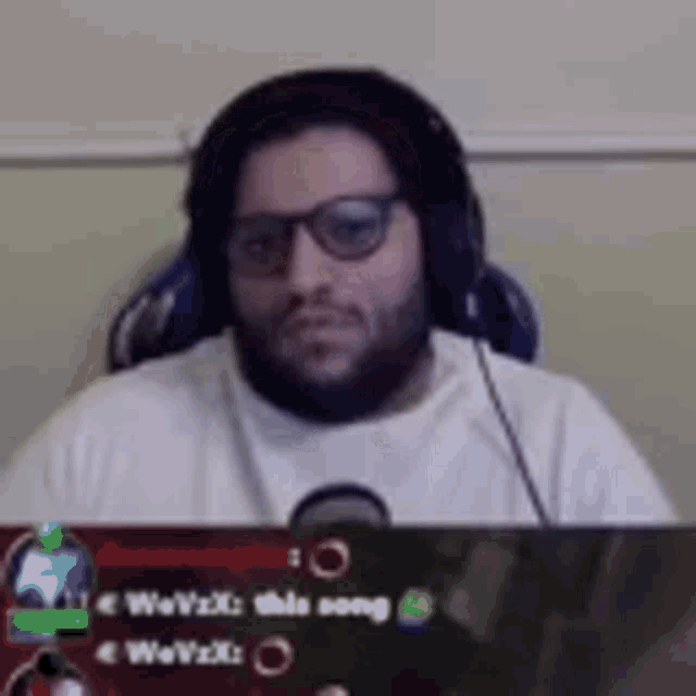 a man with a beard and glasses is wearing headphones and sitting in a chair .