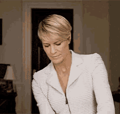 a woman in a white jacket is standing in a living room looking down .