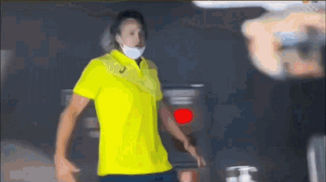 a man wearing a yellow shirt and a white mask is walking in a dark room .