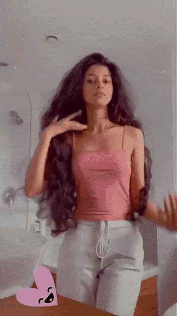 a woman in a pink tank top is standing in front of a bathroom mirror