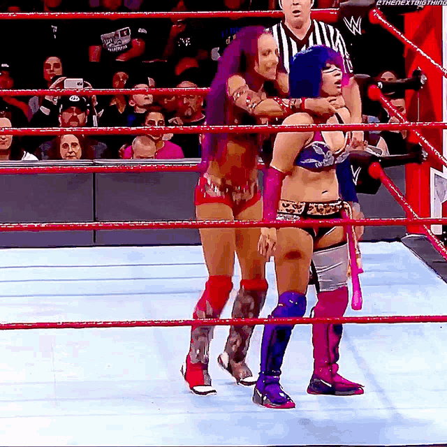 two women are wrestling in a ring with a referee watching