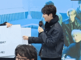 a man in a black jacket is holding a microphone in front of a sign that says ' ? '