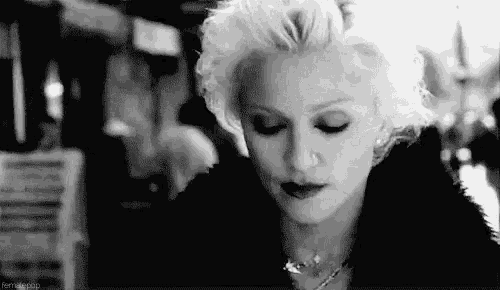 a black and white photo of a woman with blonde hair wearing a fur coat and necklace .