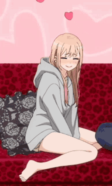 a blonde anime girl is sitting on a red couch with hearts in the background