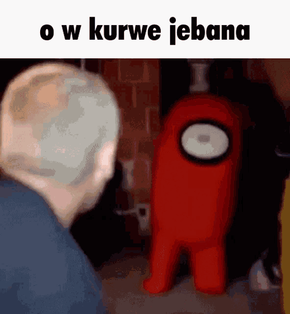a man is standing next to a red among us character in a room .