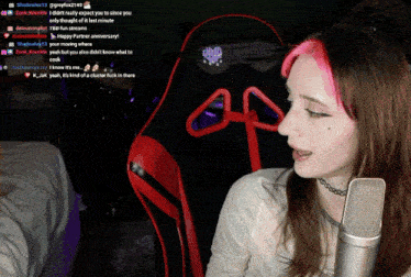 a girl with pink hair is sitting in front of a microphone and a chair that says tbd fan streams