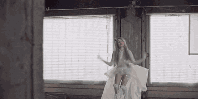 a woman in a white dress and boots is standing in front of a window .
