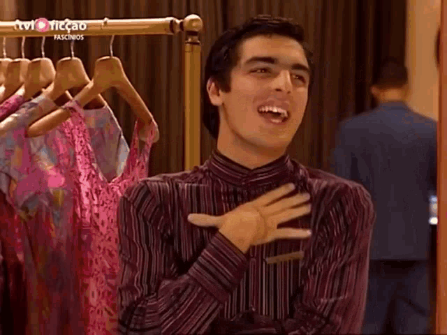 a man in a striped shirt is laughing in front of a rack of clothes that says tvi ticcao