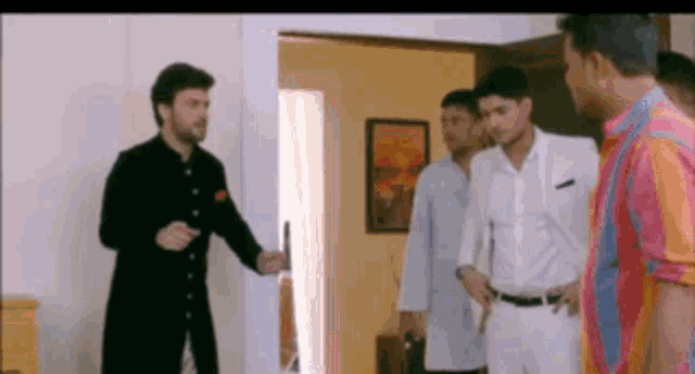 a group of men are standing in a room talking to each other . one of the men is wearing a black jacket .