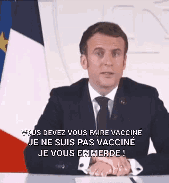 a man in a suit and tie is sitting at a desk in front of a french flag .