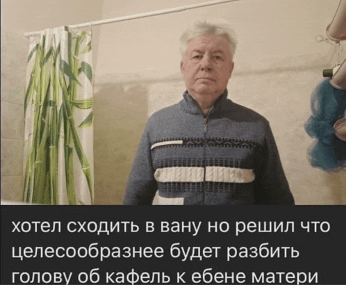 a man in a blue sweater is standing in front of a shower curtain with russian writing on it