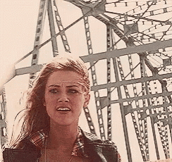 a woman wearing a plaid shirt and a leather jacket is standing in front of a fence