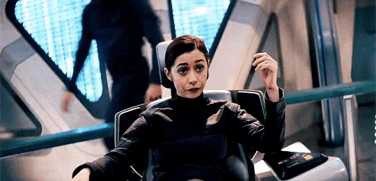 a woman is sitting in a chair with her arms outstretched and a man is walking behind her .