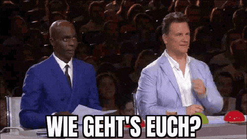 a man in a blue suit is sitting next to another man in a blue suit and tie in front of a crowd .