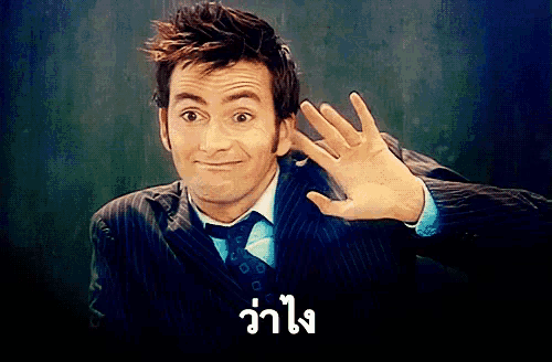 a man in a suit and tie is waving his hand in front of a sign that says วา โง