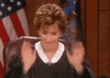 a woman in a judge 's robe is sitting in a chair in front of an american flag .