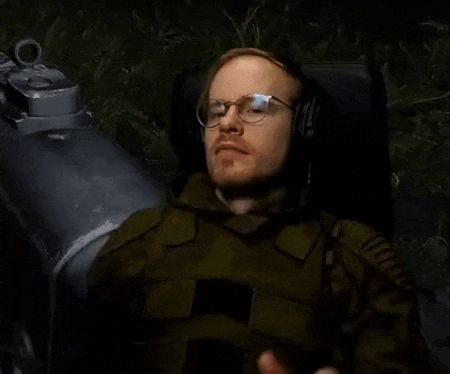 a man in a military uniform and headphones is sitting in front of a gun .