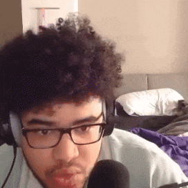a man with curly hair and glasses is talking into a microphone .