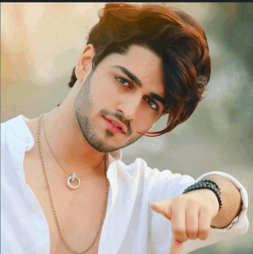 a young man wearing a white shirt and a necklace points his finger