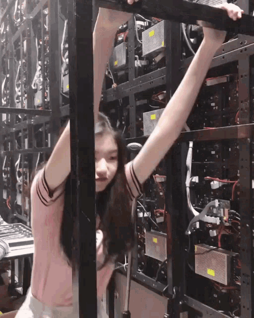 a girl in a pink shirt is hanging upside down in front of a row of servers