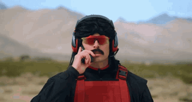 a man wearing sunglasses and headphones is talking on a cell phone in the desert .