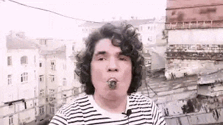 a man with curly hair is smoking a cigar while wearing a striped shirt and a microphone .