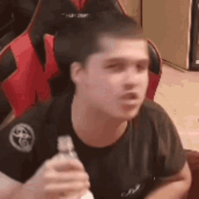 a man is sitting in a chair holding a bottle of water and making a funny face .