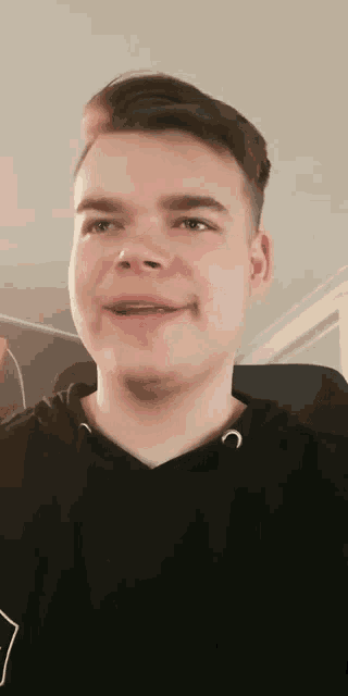 a young man wearing a black hoodie is smiling and looking at the camera