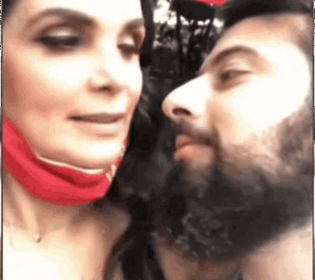 a man with a beard and a woman wearing a red mask are kissing each other .
