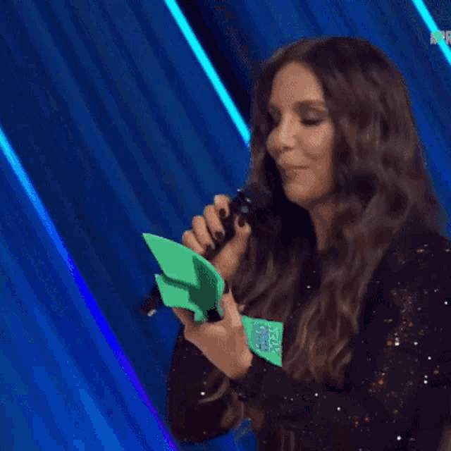 a woman holding a green trophy and a microphone that says performance do ano on it