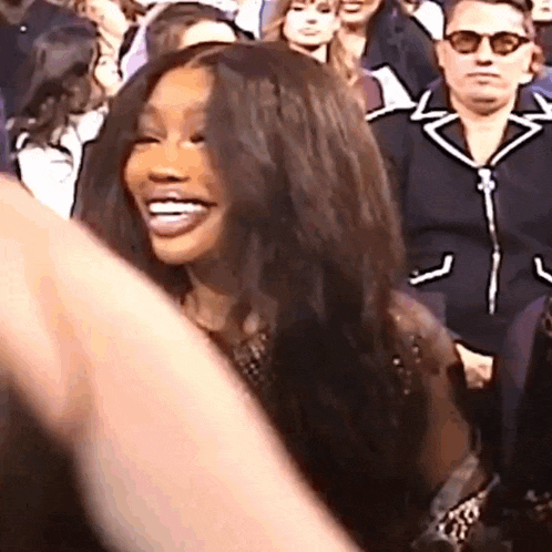 a woman with long hair is sitting in a crowd of people and smiling .