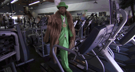 a man in a green fur coat is walking on a treadmill in a gym